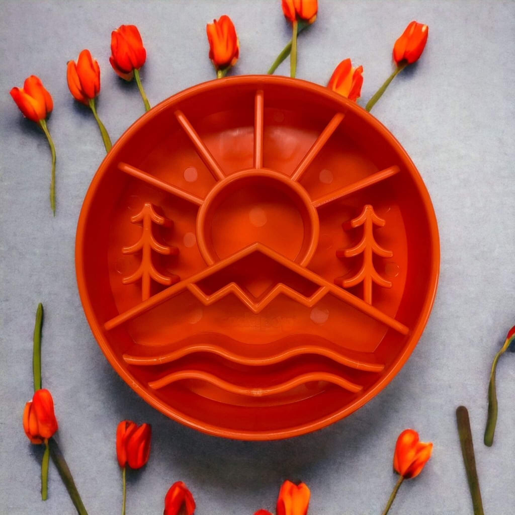 Orange slow feeder for dogs with nature design surrounded by orange flowers on a gray background