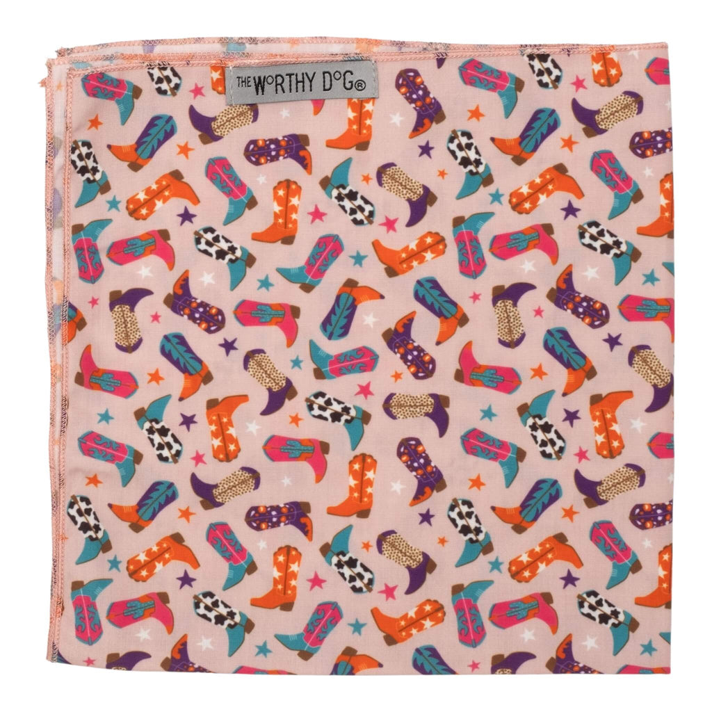 Colorful patterned dog bandana with cowboy boot design on a beige background, branded 'The Worthy Dog'.